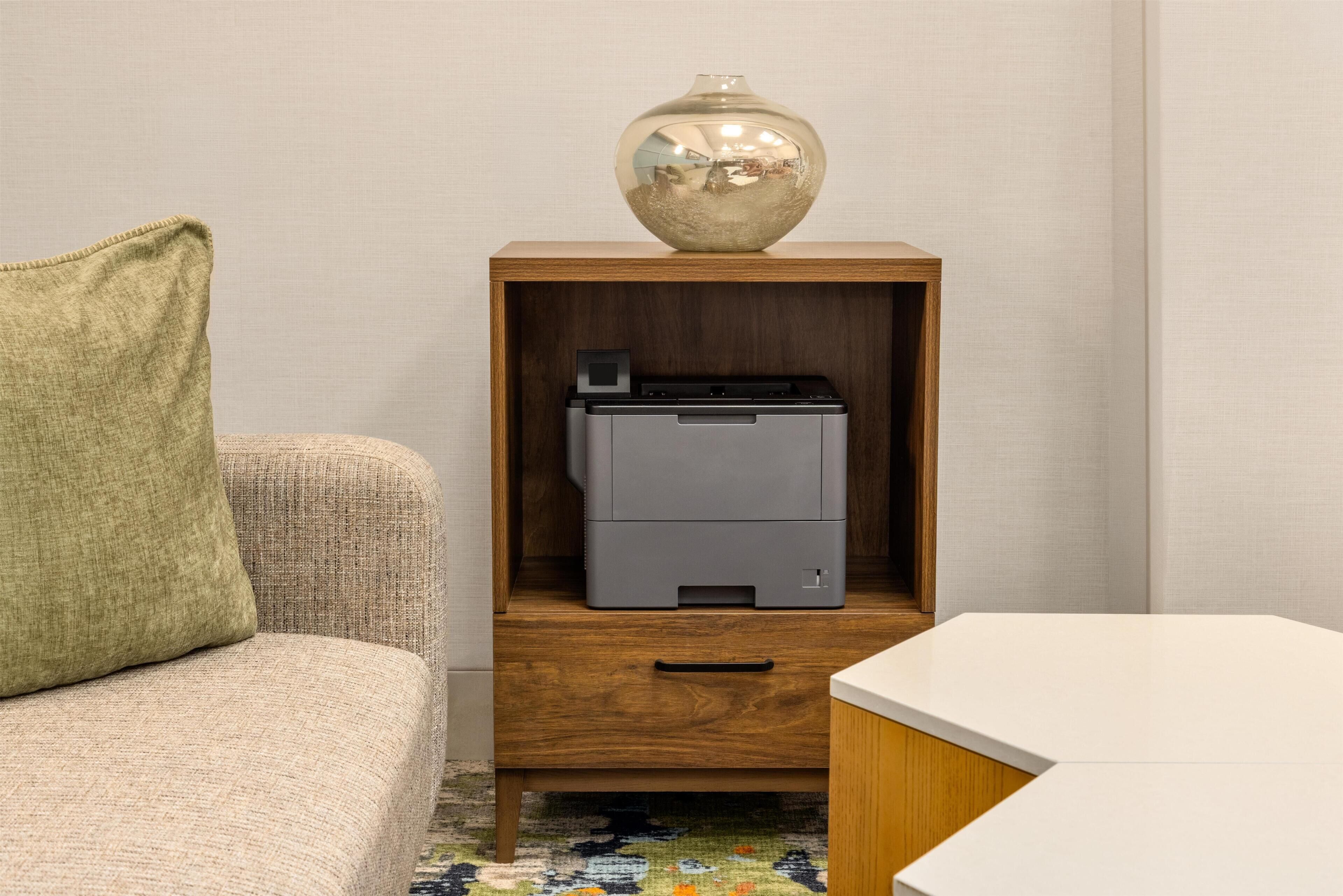 A wooden cabinet with a printer, a vase, and a cushion on a sofa.