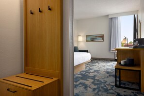 Habitación de hotel con cama, escritorio, silla, lámpara, un cuadro y vistas al exterior.