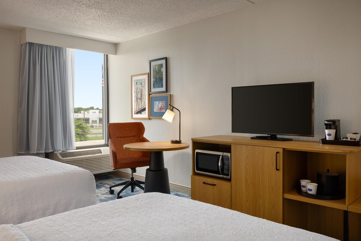 Habitación de hotel con dos camas, un escritorio con televisor, cafetera y microondas.