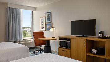 A hotel room with two beds, a desk with a TV, a coffee maker, and a microwave.