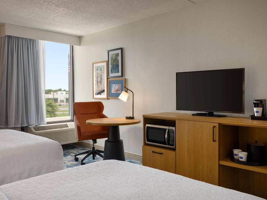 A hotel room with two beds, a desk with a TV, a coffee maker, and a microwave.