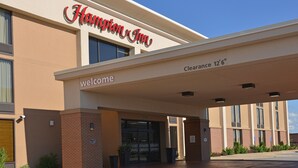 Exterior del Hampton Inn con un letrero visible, un cartel de bienvenida y un letrero con la altura máxima.