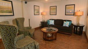 Una sala de estar con sillones estampados, un sofá oscuro, una mesa de centro de vidrio y cuadros en las paredes.