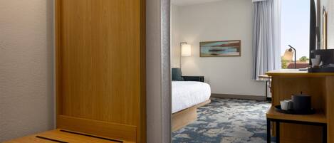 A hotel room with a bed, a desk, a chair, a lamp, a painting, and a view of the outdoors.