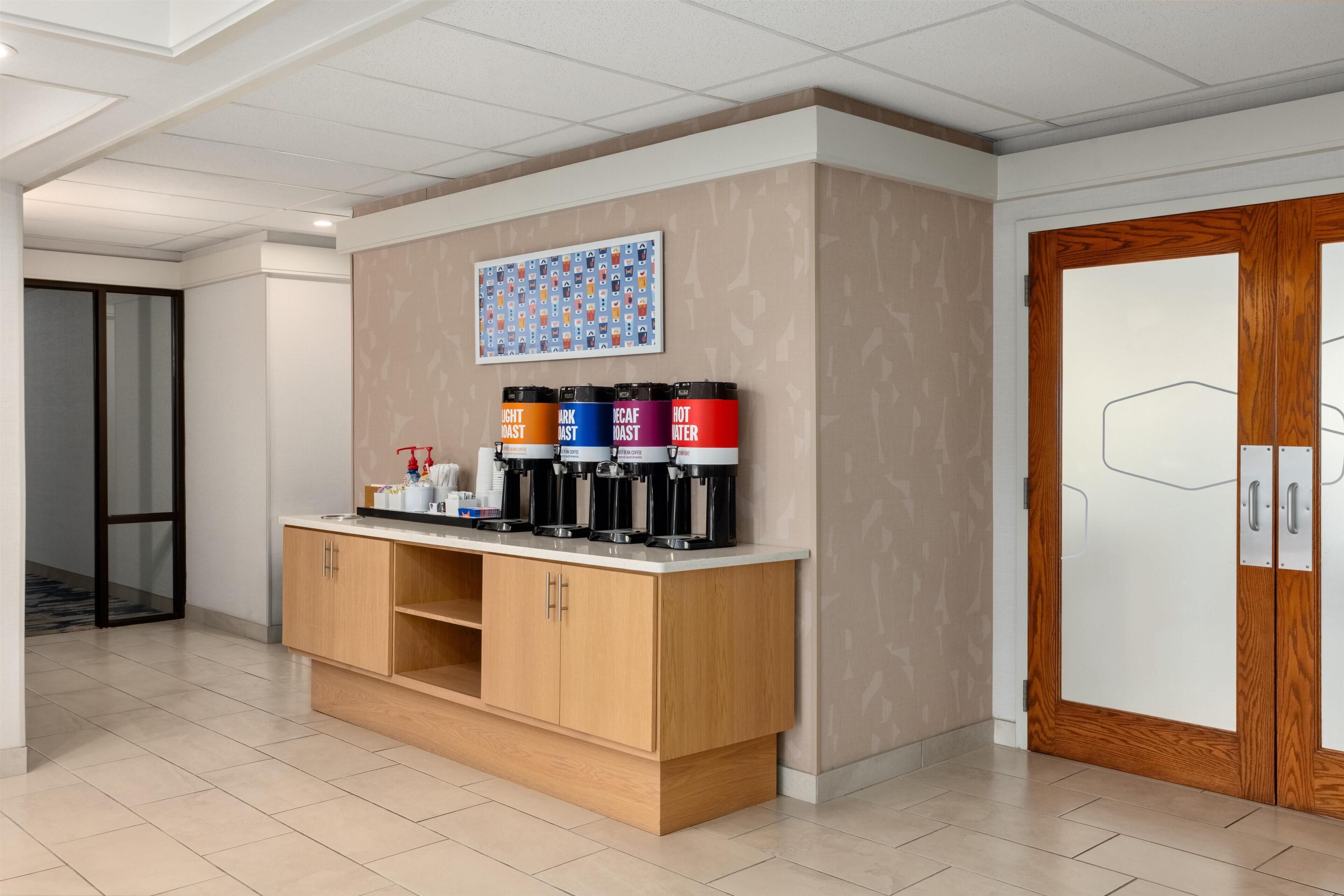 Una estación de café con cuatro dispensadores etiquetados como 'Light Roast', 'Dark Roast', 'Decaf' y 'Agua Caliente'.