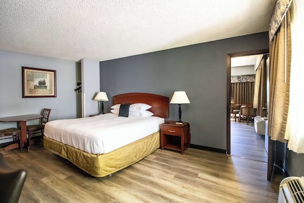 A hotel room with a bed, bedside lamps, a desk with a chair, and a framed picture on the wall.
