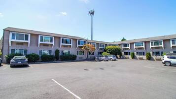A multi-story motel with a parking lot, several cars parked, and a clear sky.