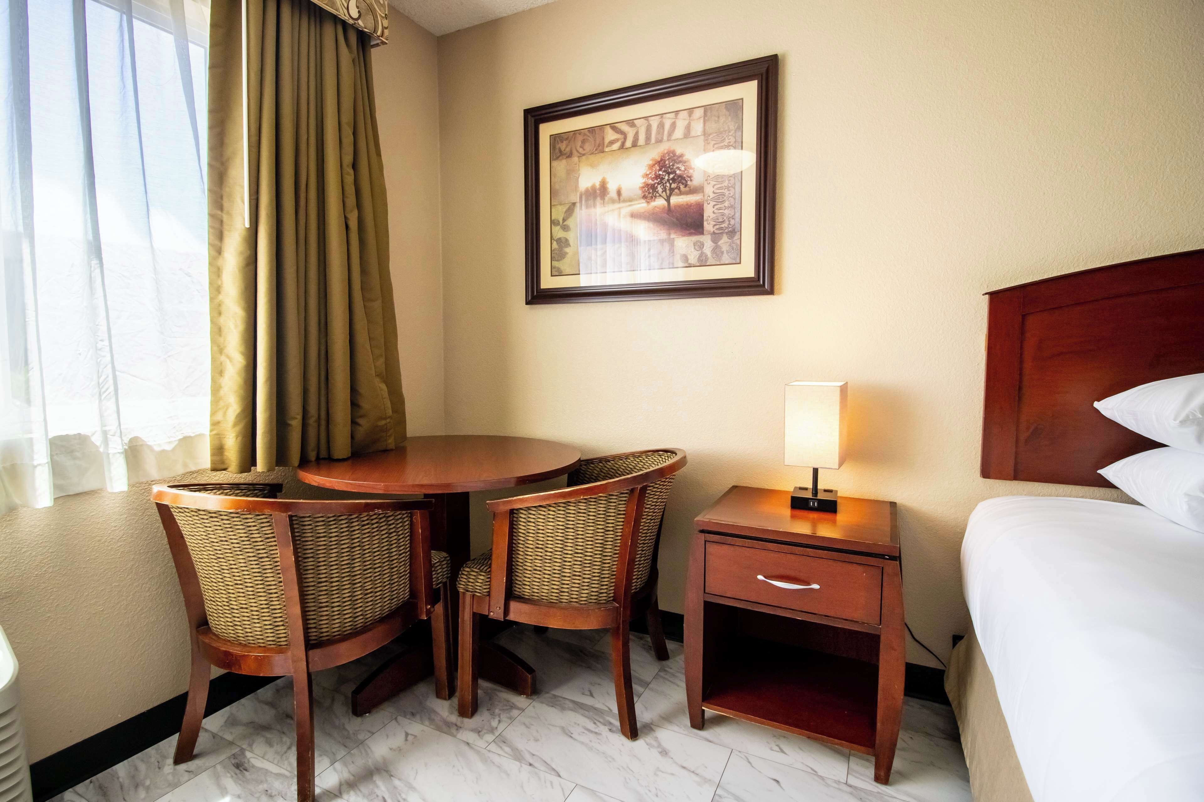 Une chambre d’hôtel avec un lit, une table de chevet, une table avec des chaises et un tableau encadré au mur.