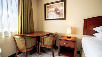 Une chambre d’hôtel avec un lit, une table de chevet, une table avec des chaises et un tableau encadré au mur.