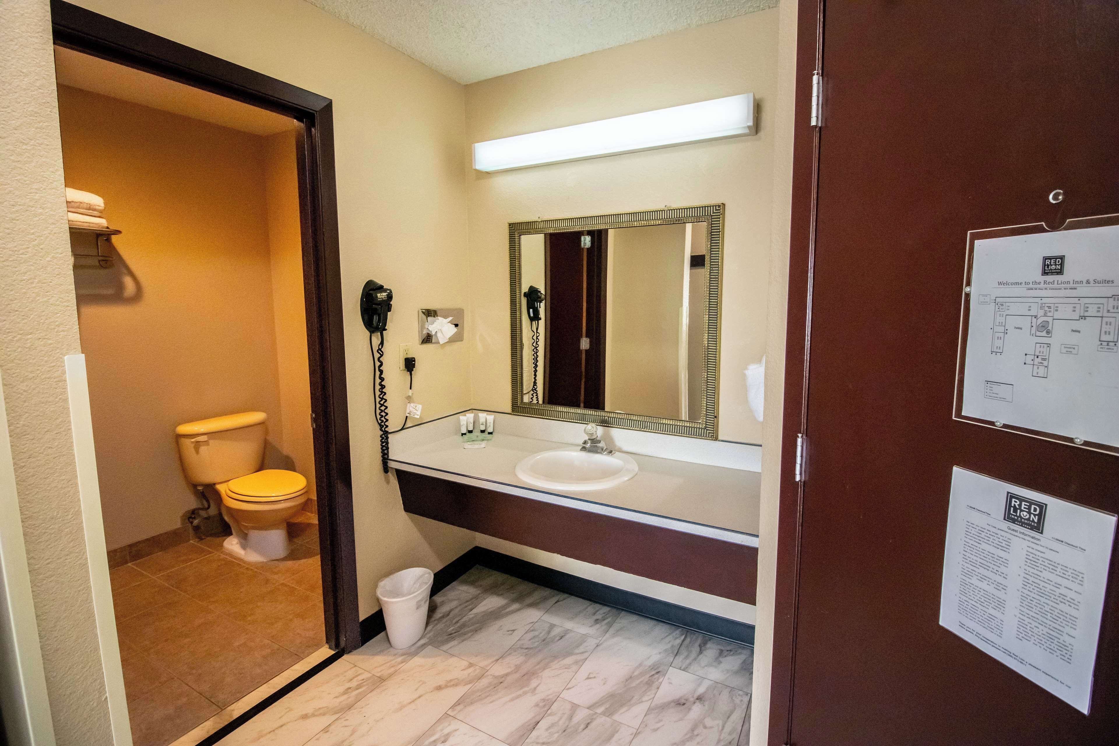 Un baño con inodoro, lavabo, espejo y un teléfono en la pared.