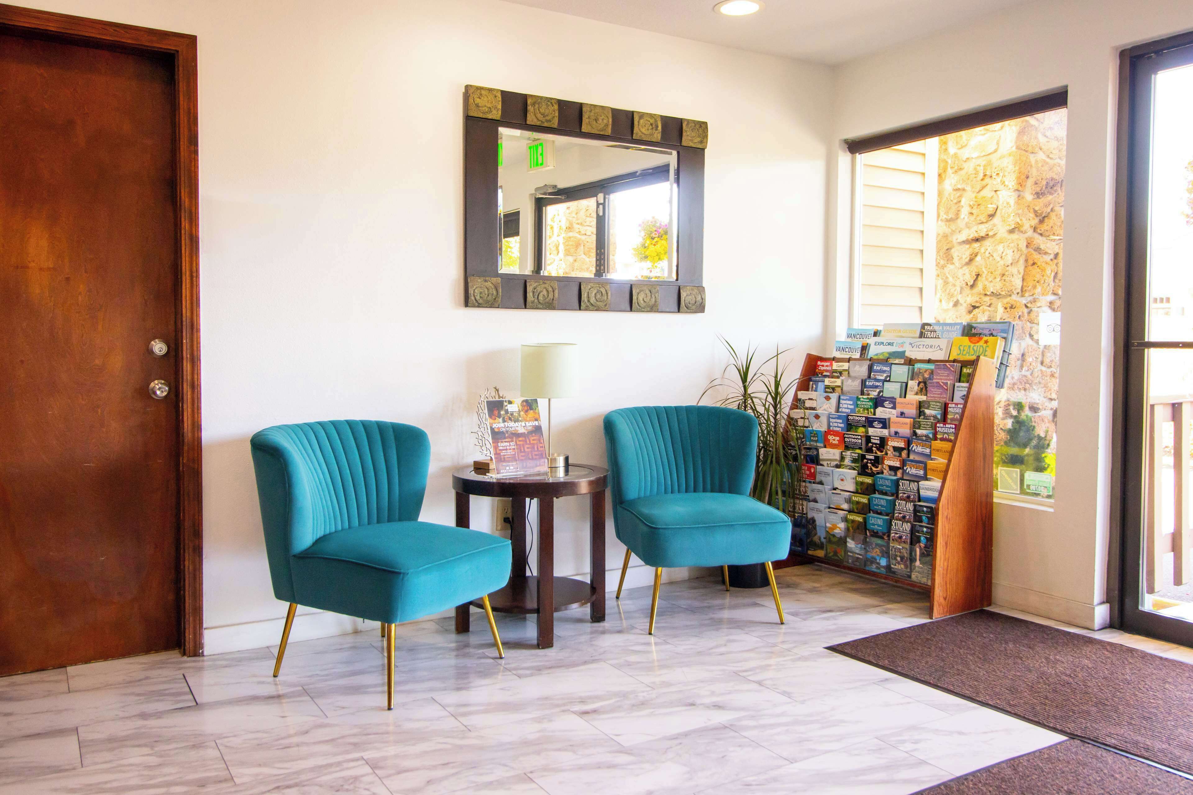 Un vestíbulo con dos sillones color turquesa, una mesita con lámpara, un espejo y un tablón de anuncios con diversos elementos.