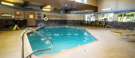 An indoor swimming pool with a clear view of the ceiling, a lifeguard chair, and a poolside area with chairs.