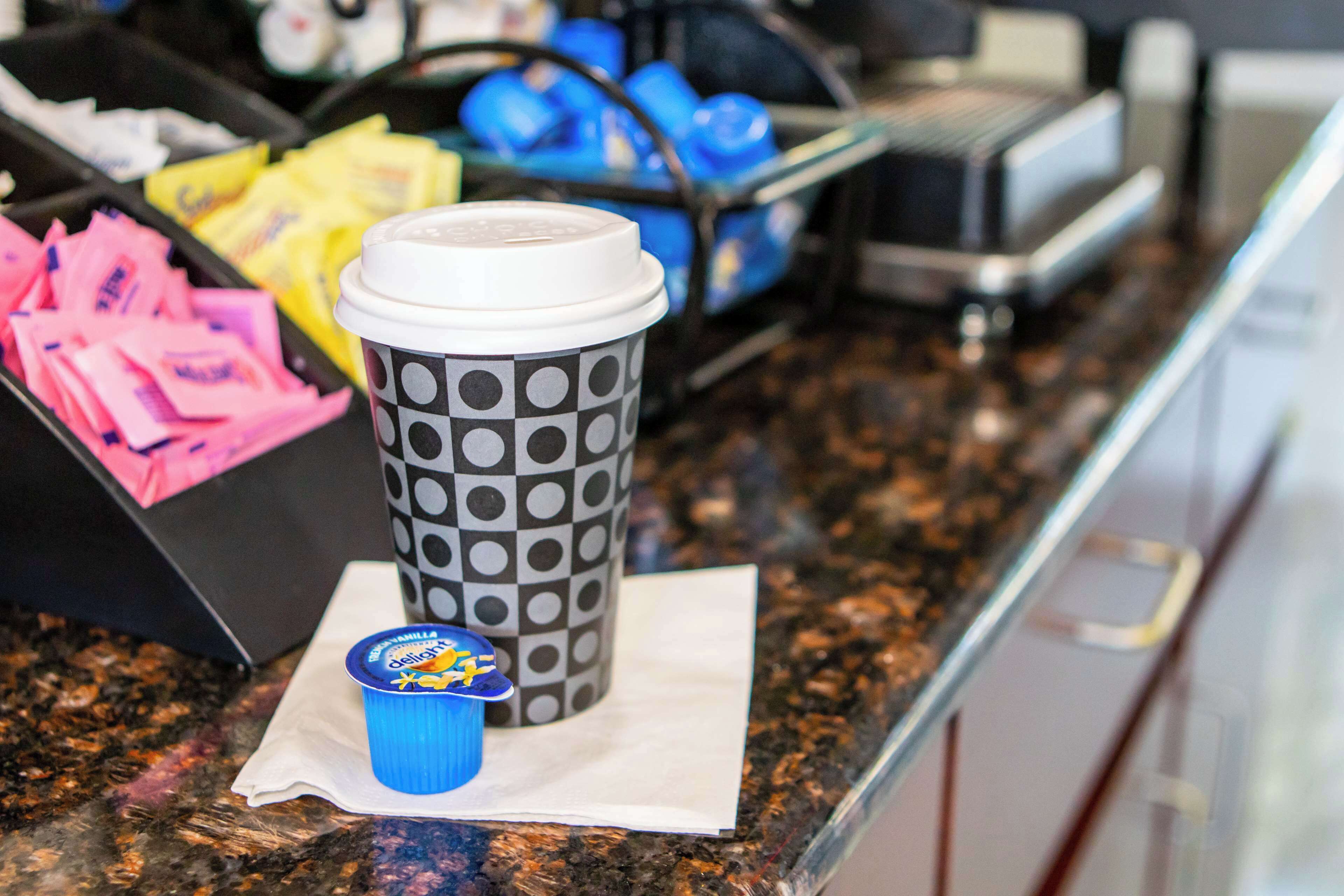 A coffee cup with a lid and a polka dot pattern, a blue cup with a lid, and a tray with pink and yellow items.