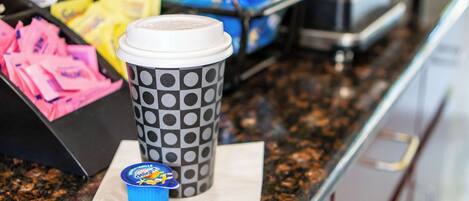 A coffee cup with a lid and a polka dot pattern, a blue cup with a lid, and a tray with pink and yellow items.