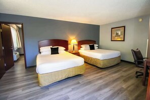 A hotel room with two beds, a desk, a chair, and a lamp.
