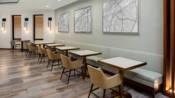 A modern dining area with wooden tables and chairs, a light-colored bench, and wall-mounted light fixtures.