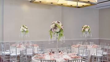 Une salle de banquet avec des tables rondes dressées pour un événement formel, agrémentée de nappes blanches, de chaises argentées et de compositions florales.