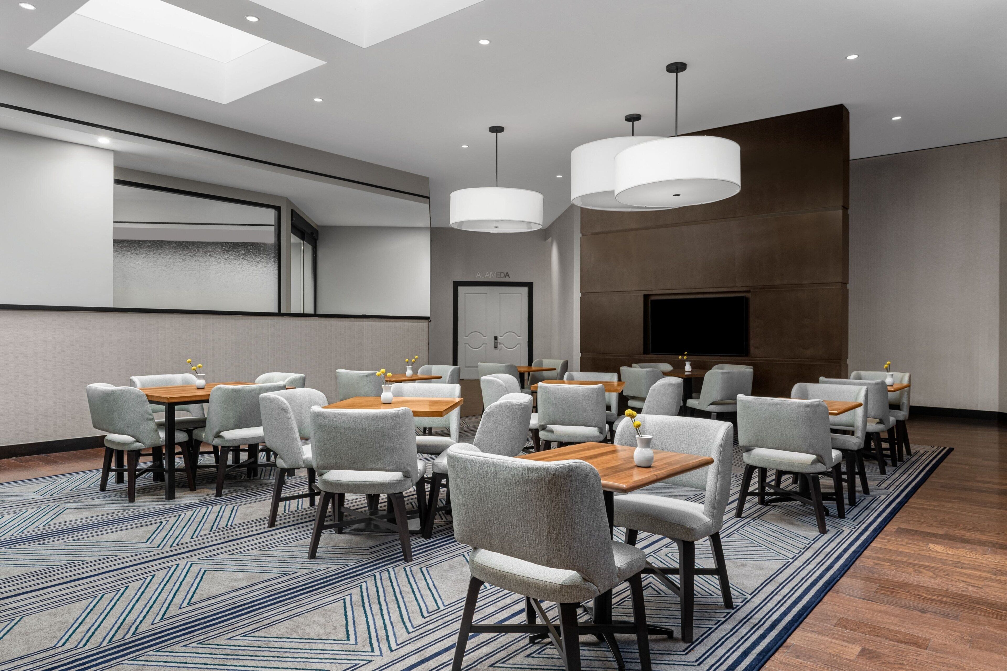 A conference room with multiple tables and chairs, a large screen, and pendant lighting.