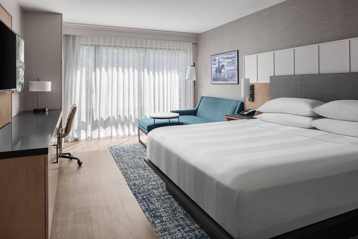 A modern hotel room with a large bed, a desk, a chair, and a television.