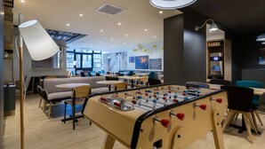 A modern indoor space with a foosball table, seating areas, and a visible staircase leading to an upper level. - ibis Styles Paris Place d'Italie Butte aux Cailles Hotel (Paris)