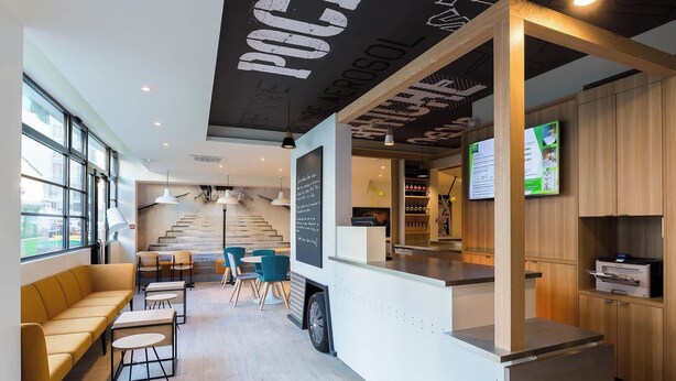 A modern cafe with a counter, seating area, and a staircase leading to an upper level. - ibis Styles Paris Place d'Italie Butte aux Cailles Hotel (Paris)