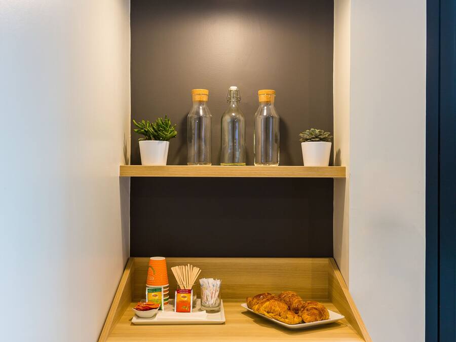 Una cocina compacta con microondas, repisa con botellas y una pequeña planta en maceta.