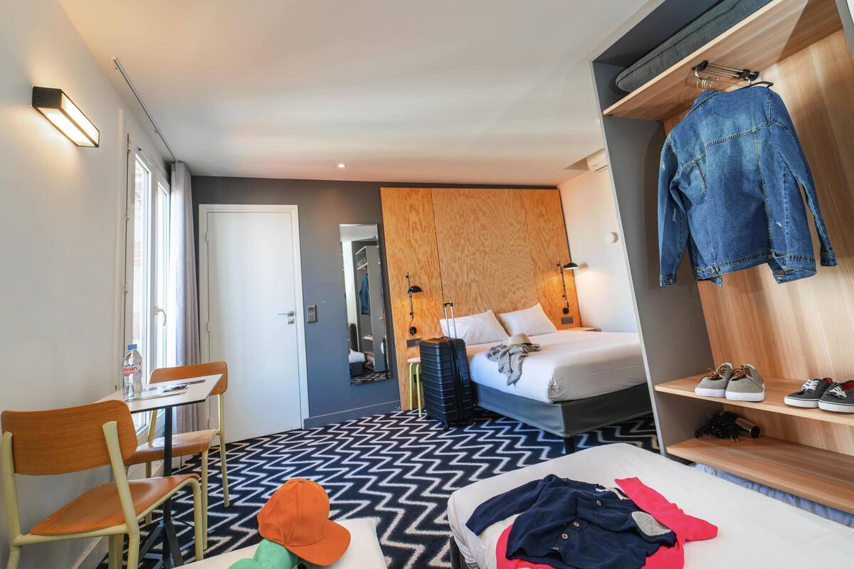 A hotel room with a bed, a desk, a chair, a wardrobe, and a mirror.