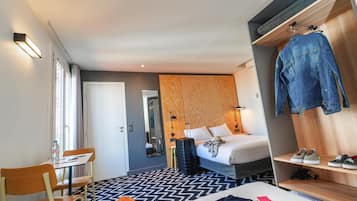 Habitación de hotel con cama, escritorio, silla, armario y espejo.