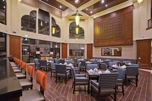 A spacious dining area with multiple tables and chairs, large windows, and a high ceiling with wooden beams. - DoubleTree by Hilton Los Angeles - Rosemead (Montebello)