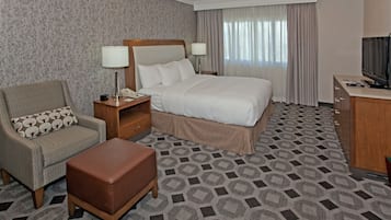 A hotel room with a bed, a chair, a desk, a television, and a patterned carpet.
