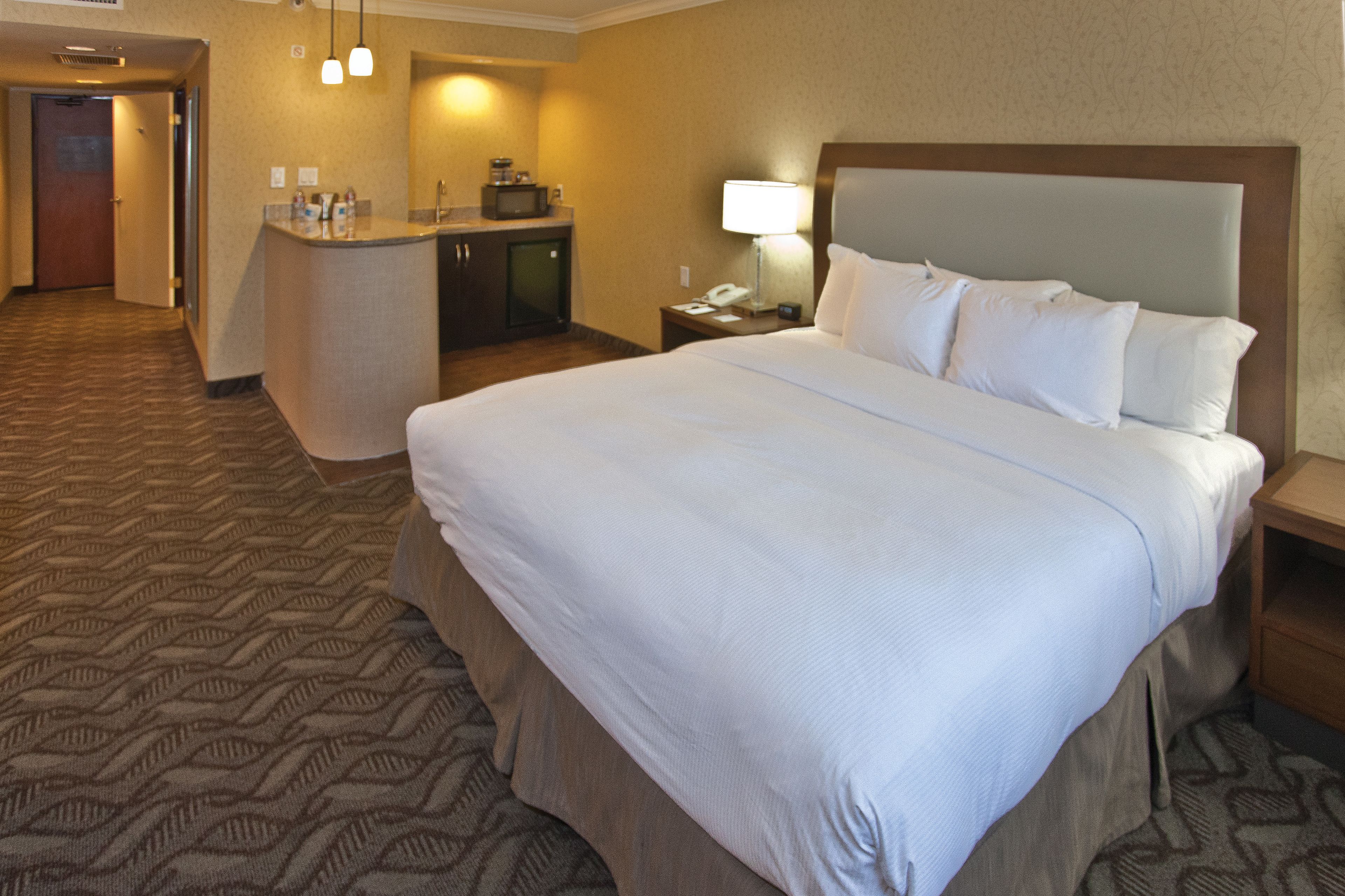 A hotel room with a large bed, a desk with a telephone, and a small kitchenette.