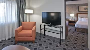 A hotel room with a television on a glass table, a sofa, a bed, and a nightstand with a lamp.