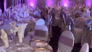 Une salle de banquet avec des tables rondes, des nappes blanches et des chaises ornées de rubans blancs.