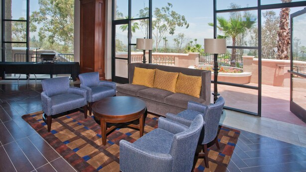 A spacious lobby with a large window offering a view of palm trees and a patio area. - DoubleTree by Hilton Los Angeles - Rosemead (Montebello)