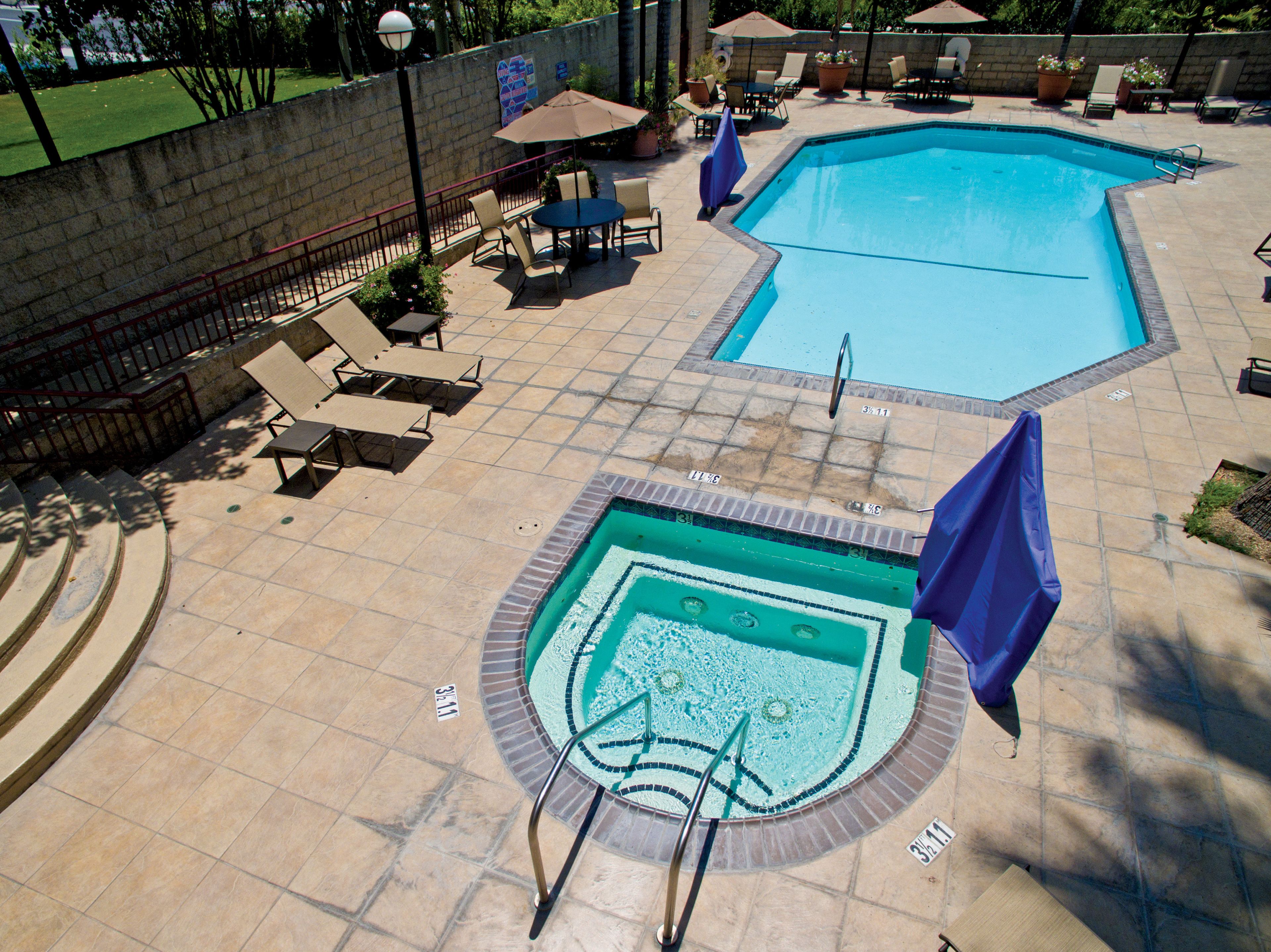 Une piscine avec une terrasse carrelée, des chaises longues et un drapeau.
