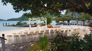 A beachside wedding setup with white chairs and a floral arch. - Catamaran Hotel Marina (Falmouth Harbour)