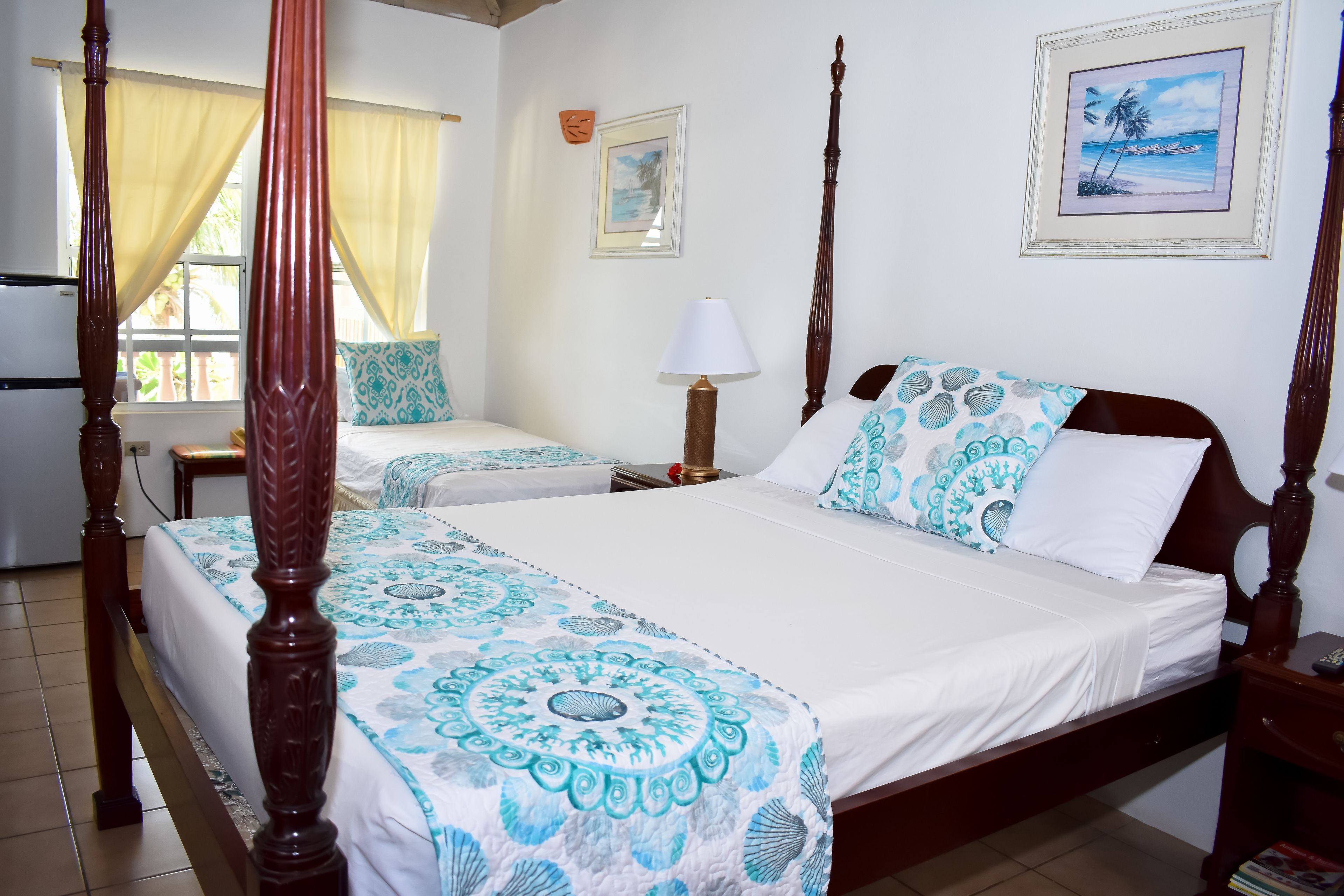A four-poster bed with a blue and white patterned bedspread, a bedside table with a lamp, and a framed picture on the wall.