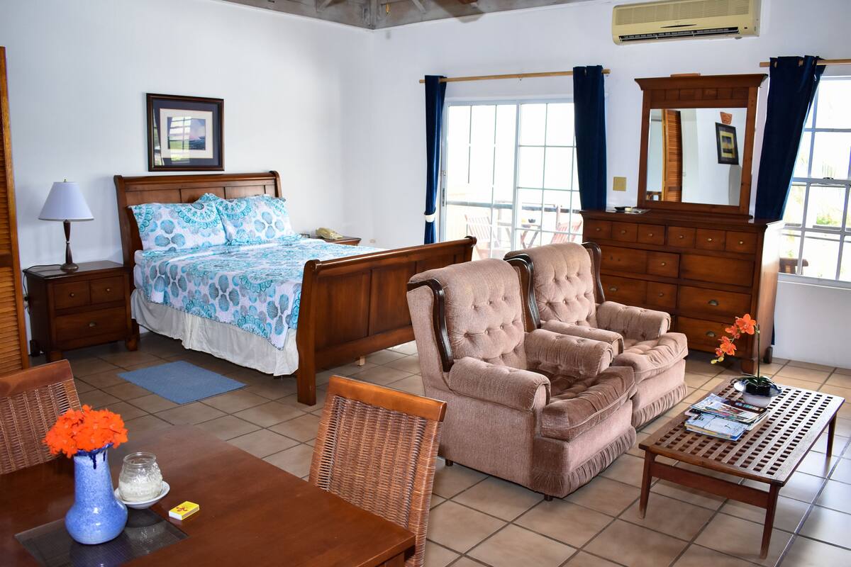 Een slaapkamer met een bed, een stoel, een tafel en een dressoir.