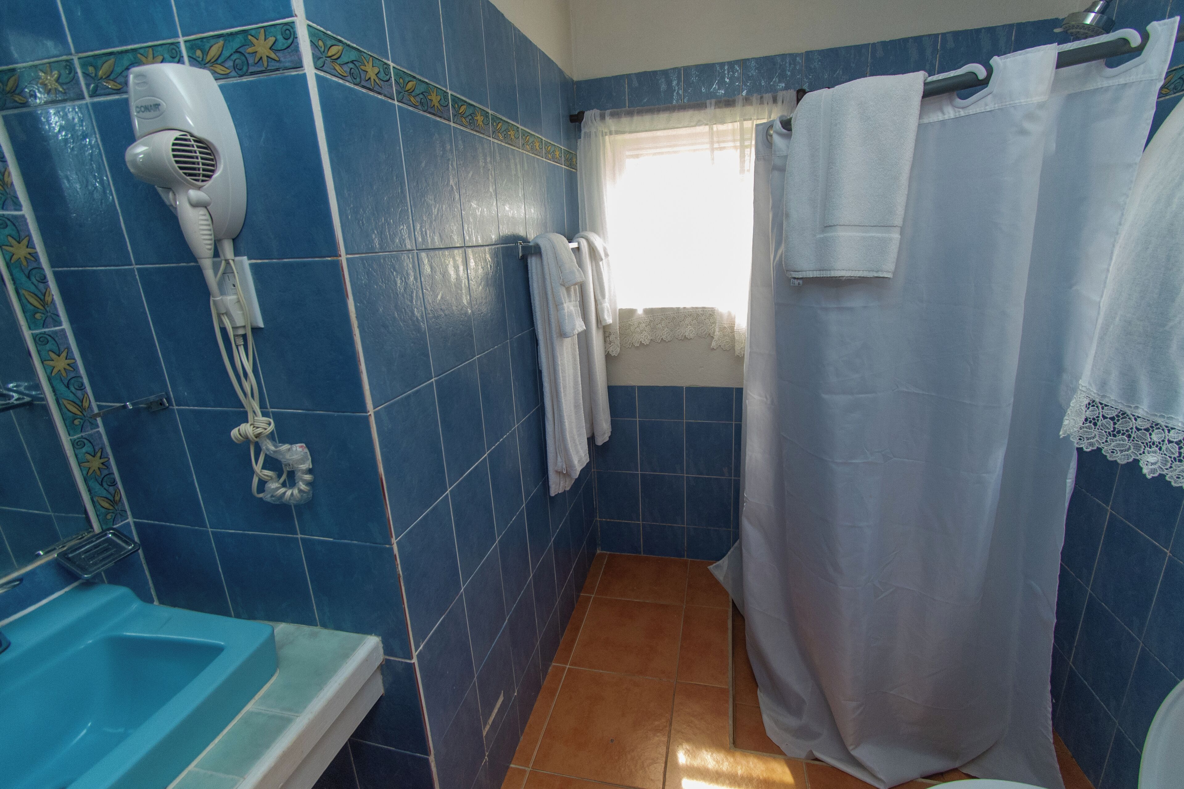 A bathroom with blue tiles, a white shower curtain, and a hairdryer on the wall.