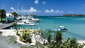 A marina with several boats docked, a small island in the background, and a building with a green roof. - Catamaran Hotel Marina (Falmouth Harbour)