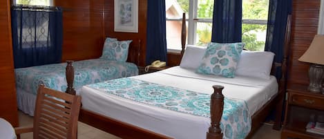 Una habitación con dos camas de madera, una silla de madera, una mesita de noche con lámpara y una ventana con cortinas.