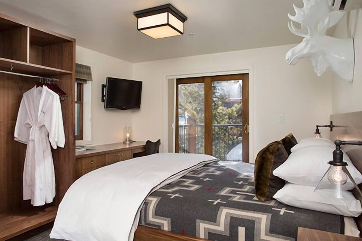 Un dormitorio con cama, armario de madera, televisor y ventana grande.