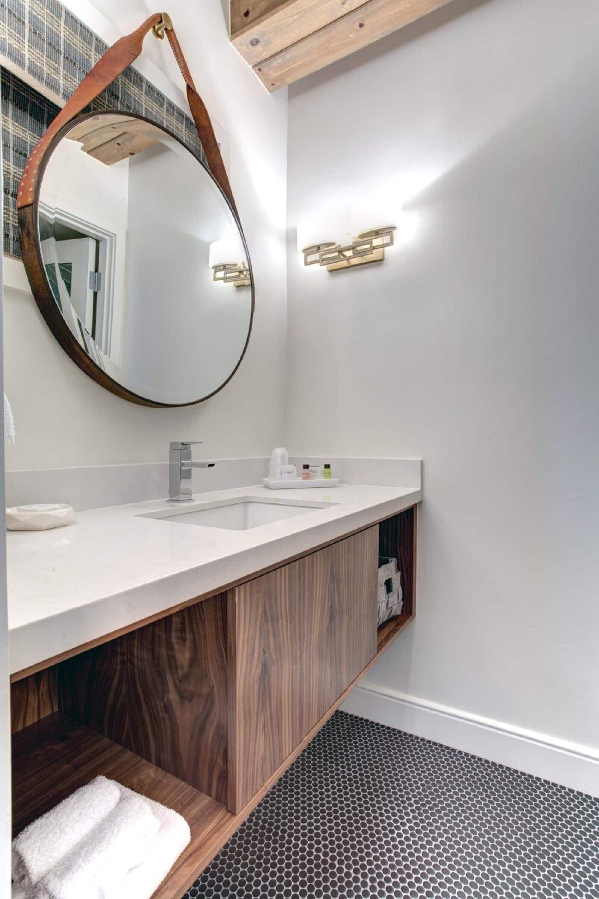 Une salle de bain moderne avec un meuble-lavabo en bois, un miroir rond et un lavabo blanc.