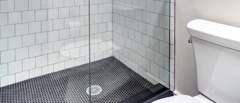 Une salle de bain moderne avec une douche à parois de verre, des murs recouverts de carreaux blancs et des toilettes blanches.