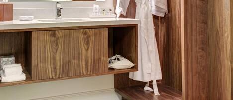 Un baño moderno con tocador de madera, un espejo grande y una bata colgada en un perchero.