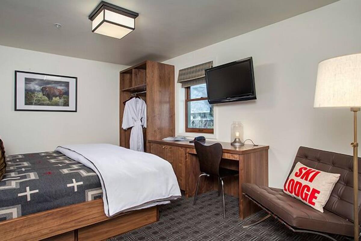 Habitación de hotel con cama, escritorio, silla, televisión y sofá con cojín.