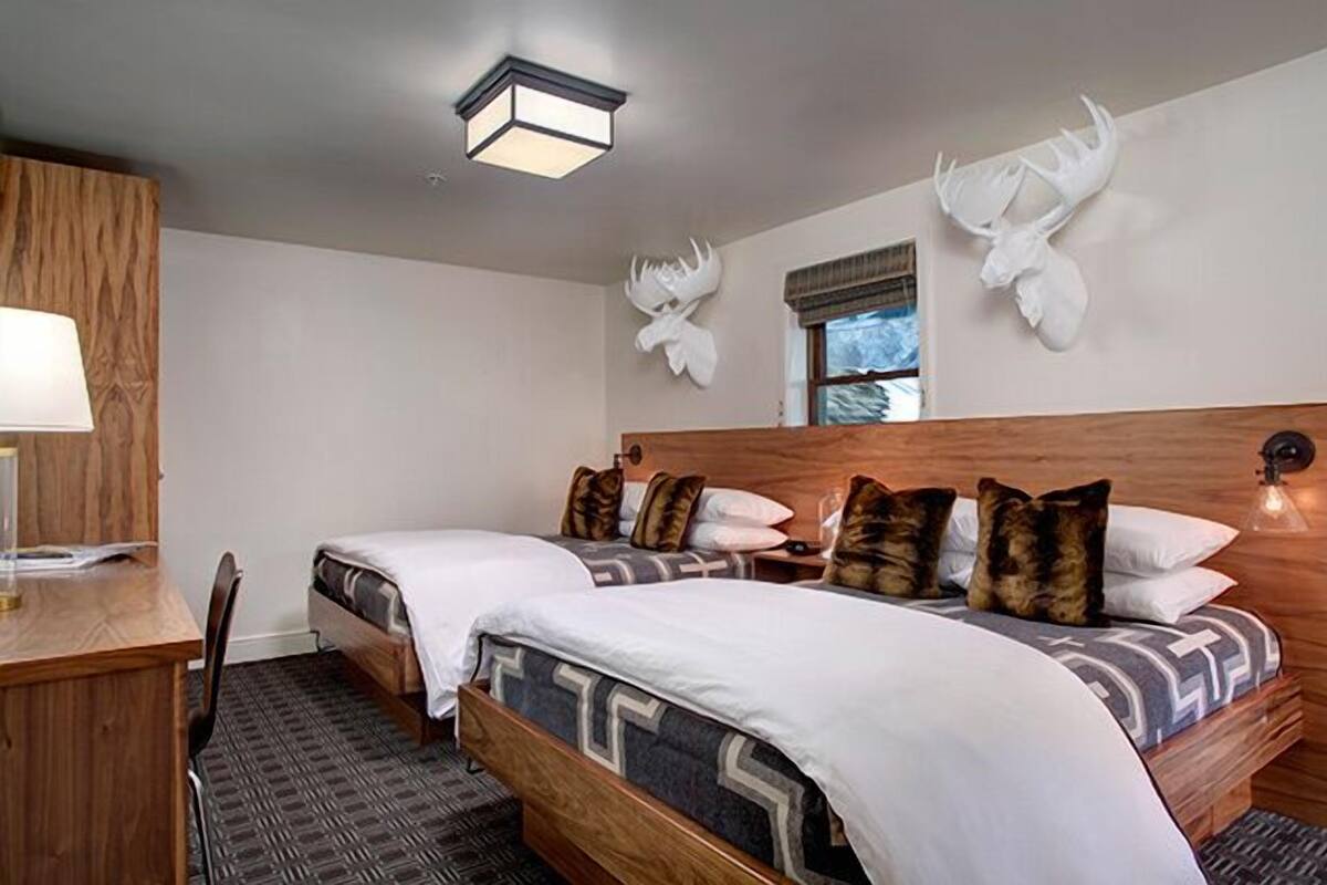 Habitación de hotel con dos camas, un escritorio y una lámpara. Hay astas decorativas en la pared.