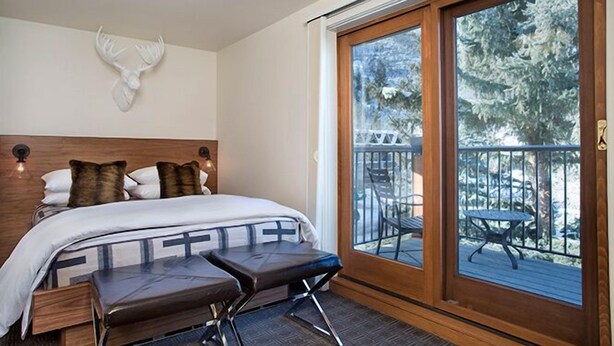 A bedroom with a large bed, a bench, and a balcony with outdoor furniture. - Hotel Durant (Aspen)