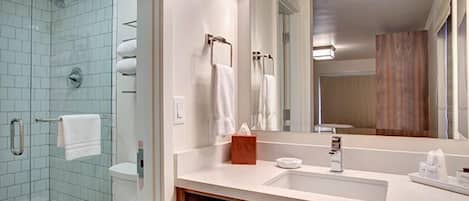 Une salle de bain avec une douche à parois de verre, des toilettes blanches, un lavabo avec un miroir et un meuble-lavabo en bois.