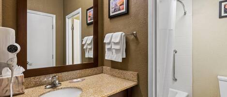 A bathroom with a granite countertop sink, a large mirror, and a shower area.